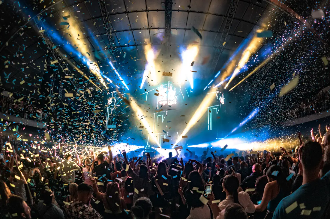 Confetti falling over a full arena crowd with blue stage beams